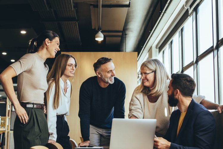 Smiling businesspeople having a discussion while collaborating on a new project in an office. Group of happy businesspeople using a laptop while working together in a modern workspace.